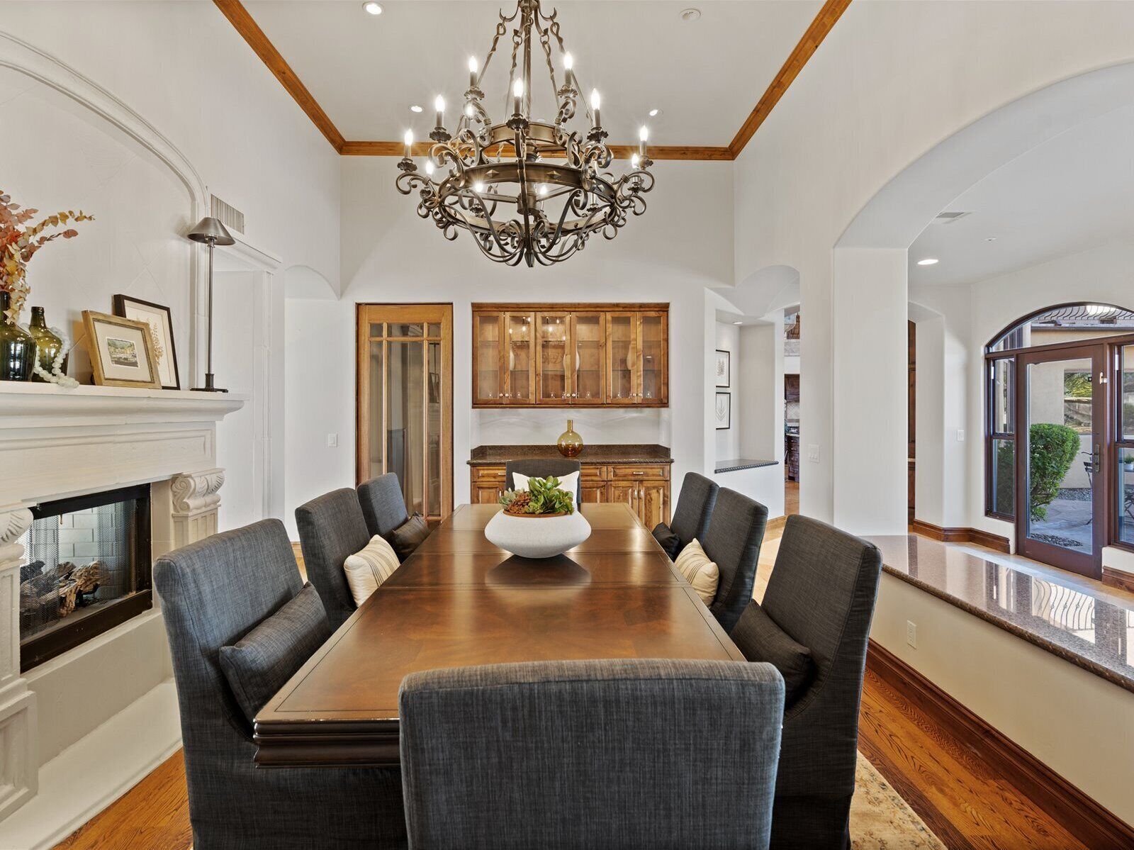 A spacious dining room with a large wooden table, six upholstered chairs, a decorative chandelier, and wooden cabinetry.