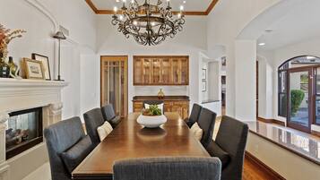 A spacious dining room with a large wooden table, six upholstered chairs, a decorative chandelier, and wooden cabinetry.