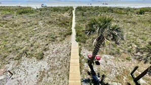A beach path leading to the ocean with a palm tree and beach chairs.