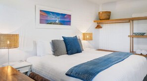 Ein Hotelzimmer mit einem Bett, zwei Nachttischen, einer Ablage und einem Wandregal mit Handtüchern sowie einem Gemälde eines Leuchtturms.