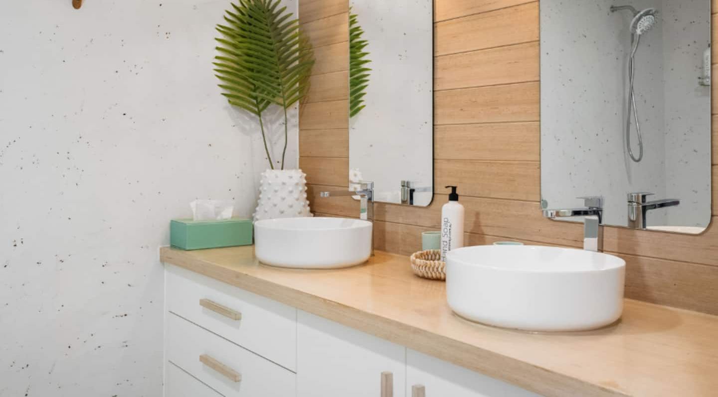 Un baño moderno con dos lavamanos, un espejo y una ducha. Hay plantas y artículos de tocador en la encimera.