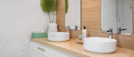 Un baño moderno con dos lavamanos, un espejo y una ducha. Hay plantas y artículos de tocador en la encimera.