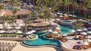 A resort with multiple swimming pools, sun loungers, and palm trees.