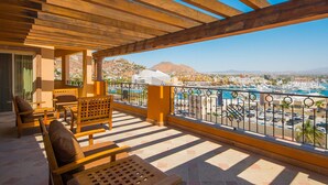 A balcony with wooden furniture, a view of a marina, and a mountainous backdrop.