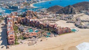 An aerial view of a coastal resort with multiple buildings, a beachfront, and a marina.