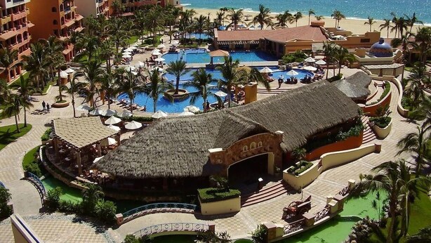 A resort with multiple swimming pools, a beach, and a thatched-roof building.