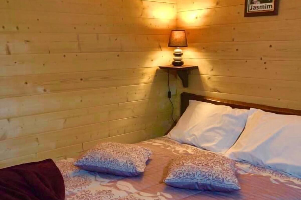 A wooden cabin room with a bed, two pillows, a lamp, and a poster on the wall.