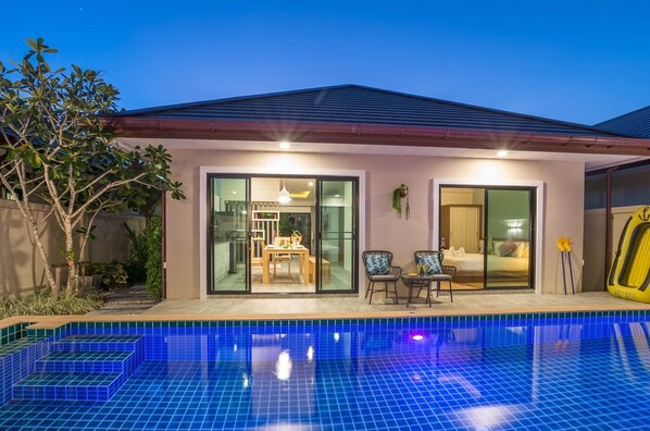 Una casa moderna con piscina, amplias puertas de vidrio que dan a un comedor, e un flotador amarillo.
