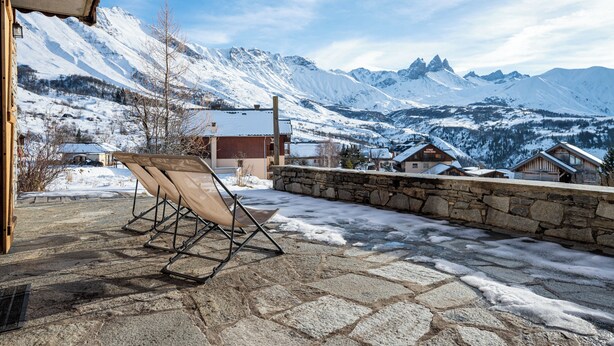 Paisaje nevado de montaña con un patio de piedra y una silla de descanso.