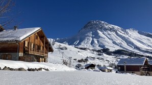 Un chalet de madera con base de piedra, un telesilla al fondo y una montaña cubierta de nieve.