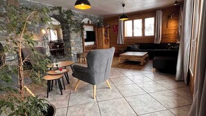 Un interior acogedor con paredes de piedra, una chimenea de piedra, un sillón gris y una mesa de comedor de madera.