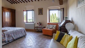 A room with a bed, a sofa, a small table with a vase, and two windows offering a view of trees. - Torriano 4 (San Casciano Val di Pesa)