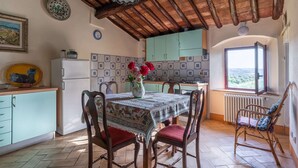 A rustic kitchen with a tiled backsplash, wooden ceiling beams, and a dining area with a table set for two. - Torriano 4 (San Casciano Val di Pesa)