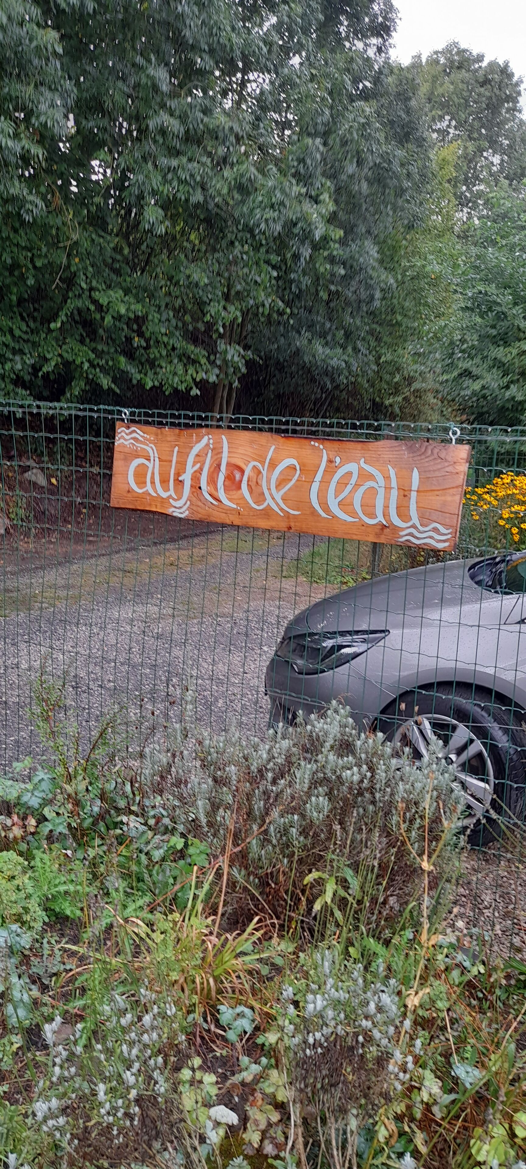 A wooden sign with the text "afrique leau" behind a wire fence, with a car parked in front.