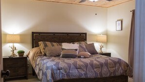 A bedroom with a wooden bed, two bedside tables, a nightstand, and a wall-mounted lamp.
