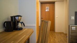 Et tekøkken med kaffemaskine, et træbord og en dør til et andet rum.