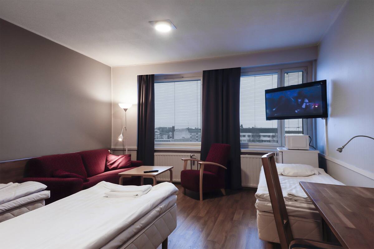 Une chambre d’hôtel avec un lit, un canapé rouge, une chaise en bois, une petite table et un téléviseur fixé au mur.