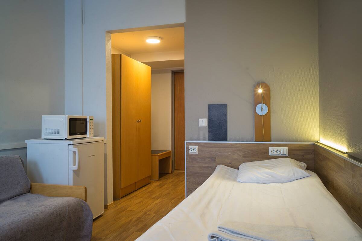 Une chambre d’hôtel compacte comprenant un lit, une petite kitchenette équipée d’un four à micro-ondes, une armoire en bois et une table de chevet.