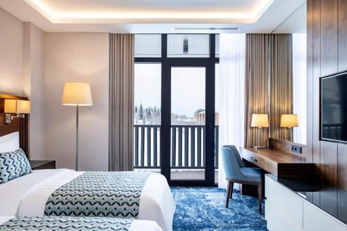 A hotel room with a bed, desk, chair, TV, and a balcony with a view.
