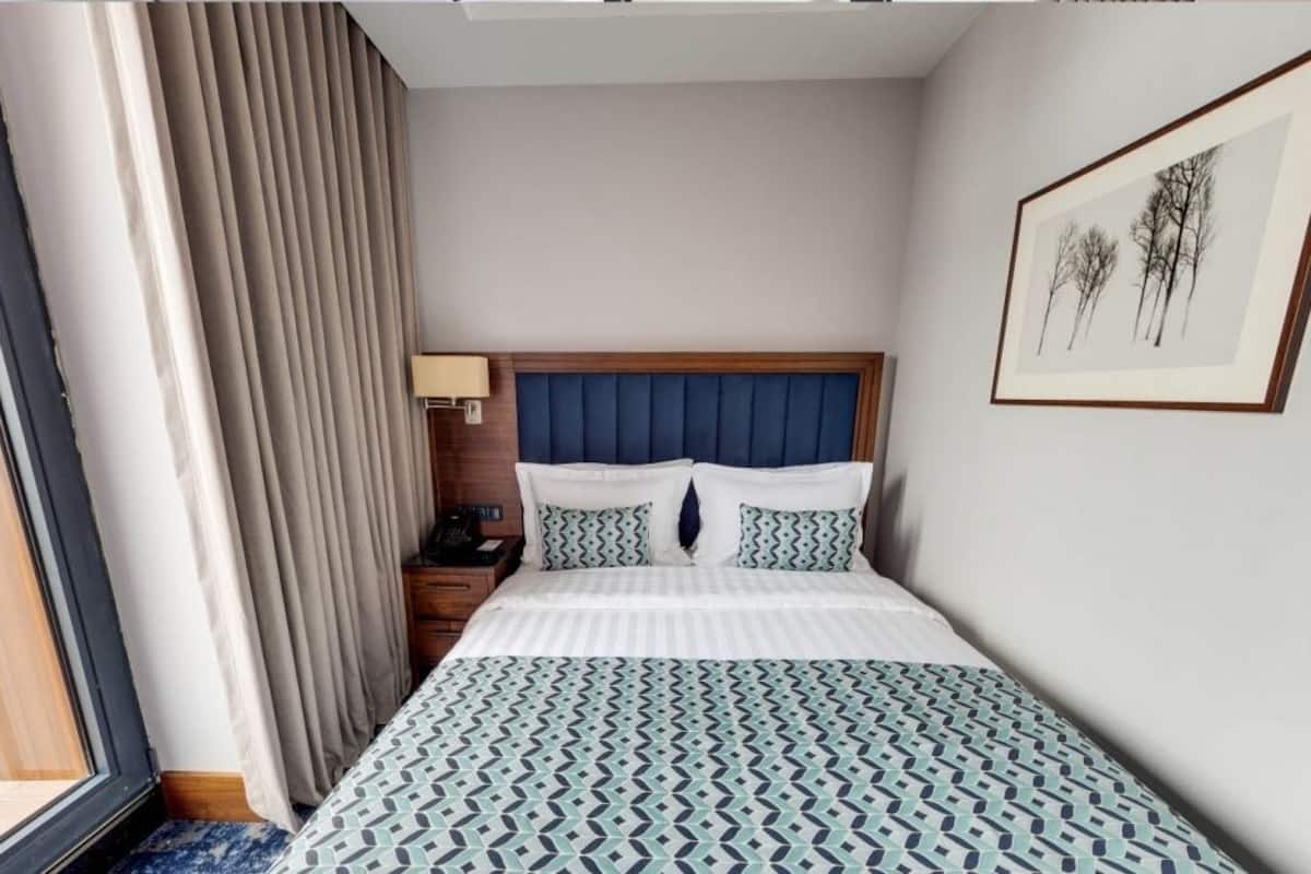 A hotel room with a bed, a nightstand, a lamp, and a framed picture on the wall.