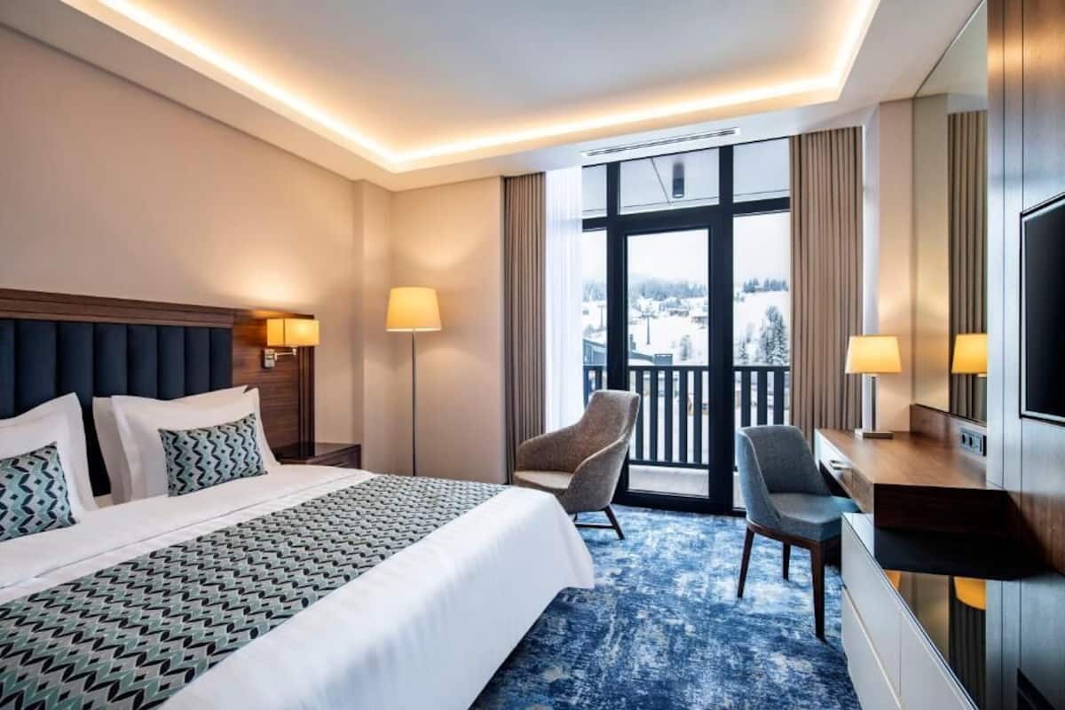 A hotel room with a large bed, two chairs, a desk, and a TV.