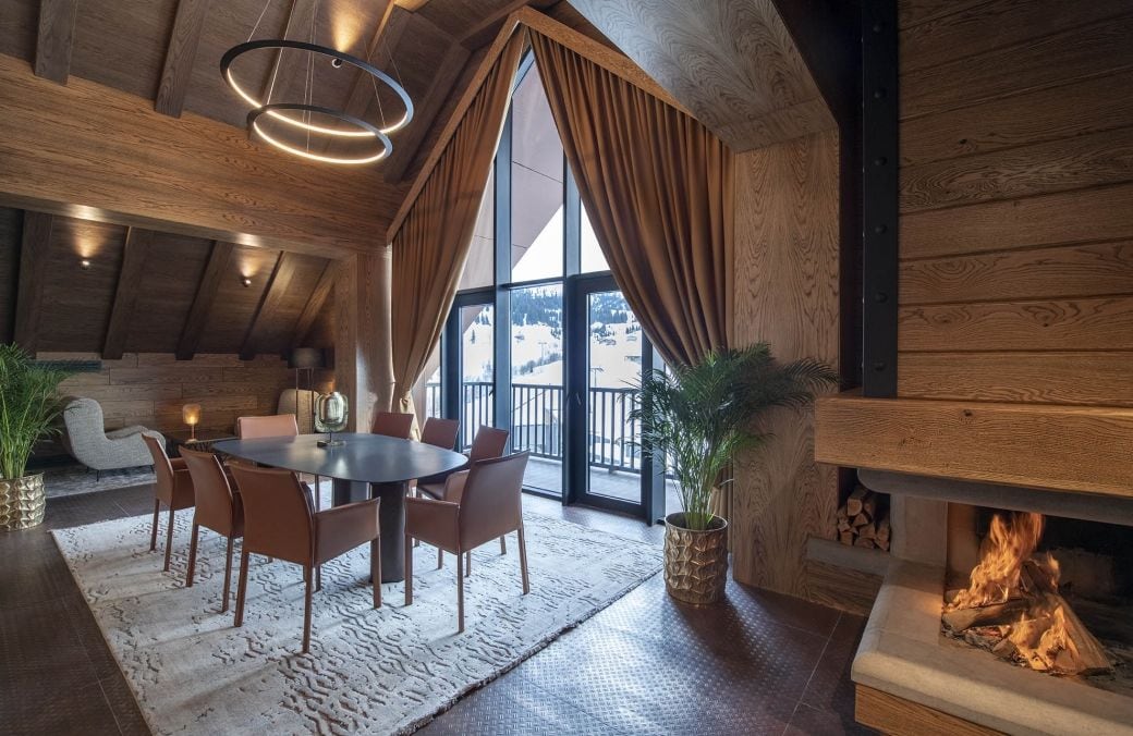 Un comedor acogedor con una mesa, sillas, chimenea y un ventanal con cortinas.