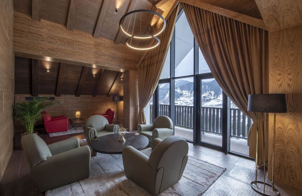 A cozy lounge area with a large window, wooden ceiling beams, and comfortable seating.