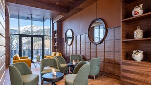Eine moderne Lounge mit grünen Polstersesseln, Holzboden und großen Fenstern mit Blick auf die Berge.