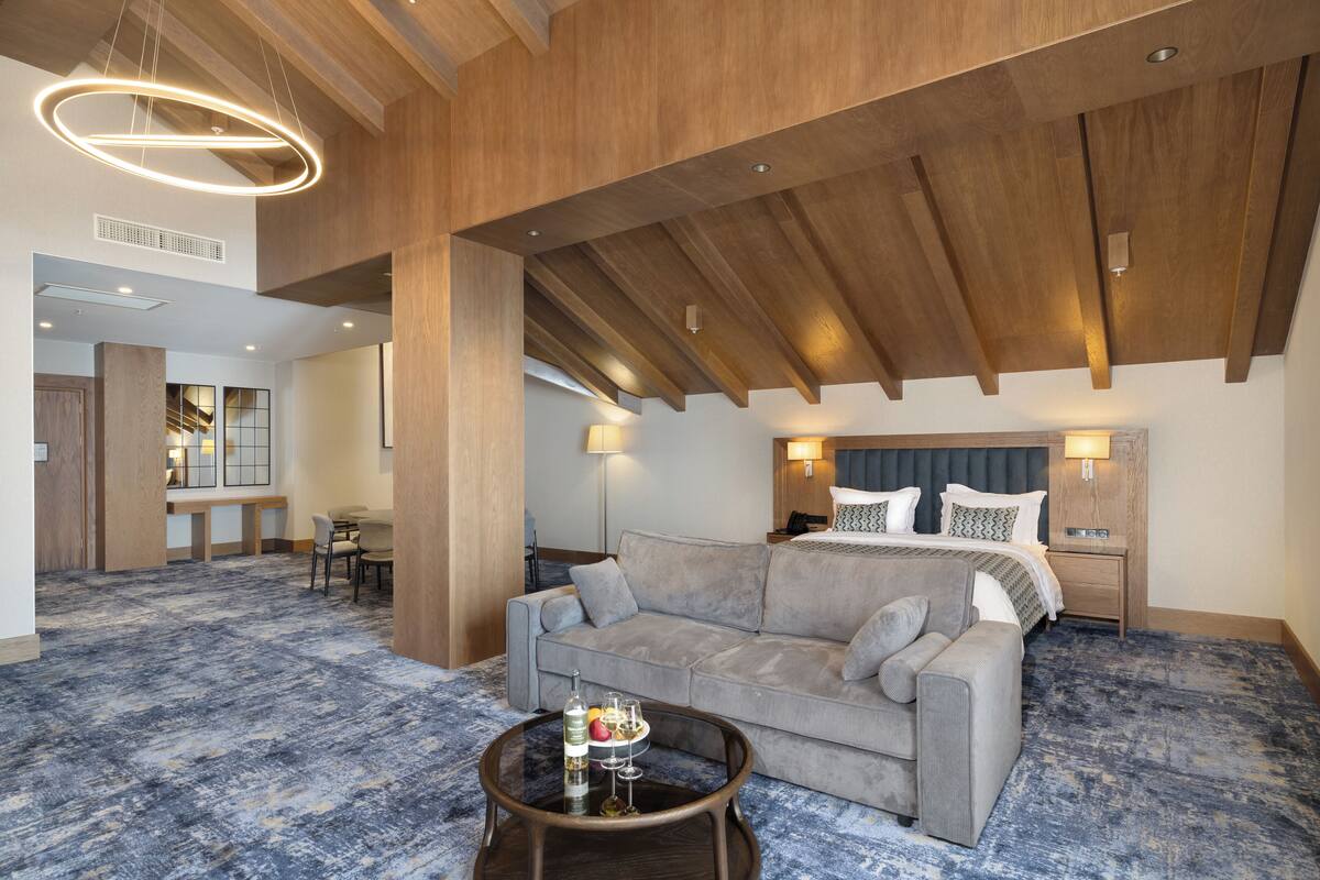 A hotel room with a large bed, a sofa, a coffee table with a tray, and a wooden ceiling.