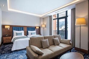 A hotel room with a large bed, a sofa, a nightstand, and a window with a view.