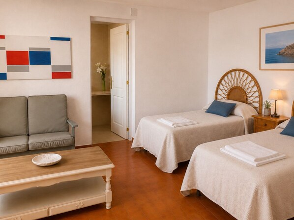 A hotel room with two beds, a sofa, a wooden table, and a painting on the wall.