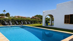 Une piscine d’un bleu éclatant, dotée de chaises longues, et un bâtiment blanc orné d’une fenêtre en arc de cercle.