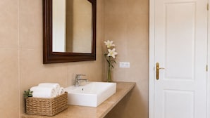 Une salle de bain avec un lavabo blanc, un miroir, un vase avec une fleur et un panier rempli de serviettes.