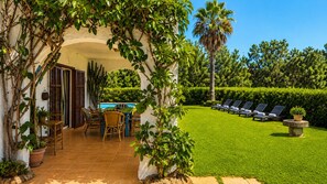 A patio with a dining table and chairs, a poolside area with lounge chairs, and a well-maintained lawn.