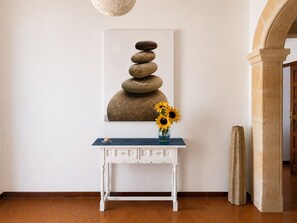 A white console table with a vase of sunflowers and a framed artwork of stacked stones on the wall.