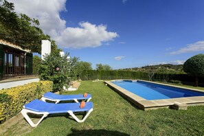 Ein Swimmingpool mit zwei blauen Liegestühlen, umgeben von gepflegtem Rasen und Hecken.