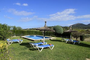 A pool area with lounge chairs and a thatched umbrella, surrounded by well-maintained grass and hedges.