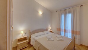 A bedroom with a bed, bedside lamps, a nightstand, and a window with curtains. - Appartamenti Badus con piscina (Badesi)