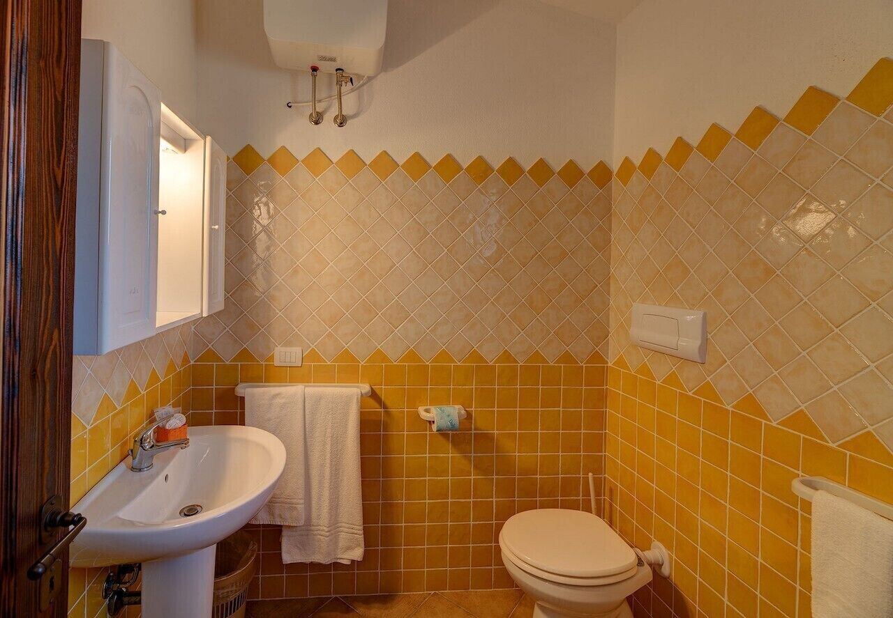 Un baño con baldosas amarillas y blancas, un lavamanos, un inodoro y un perchero para toallas.