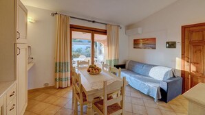 A dining area with a table set for two, a sofa, and a view of the outdoors through a window. - Appartamenti Badus con piscina (Badesi)