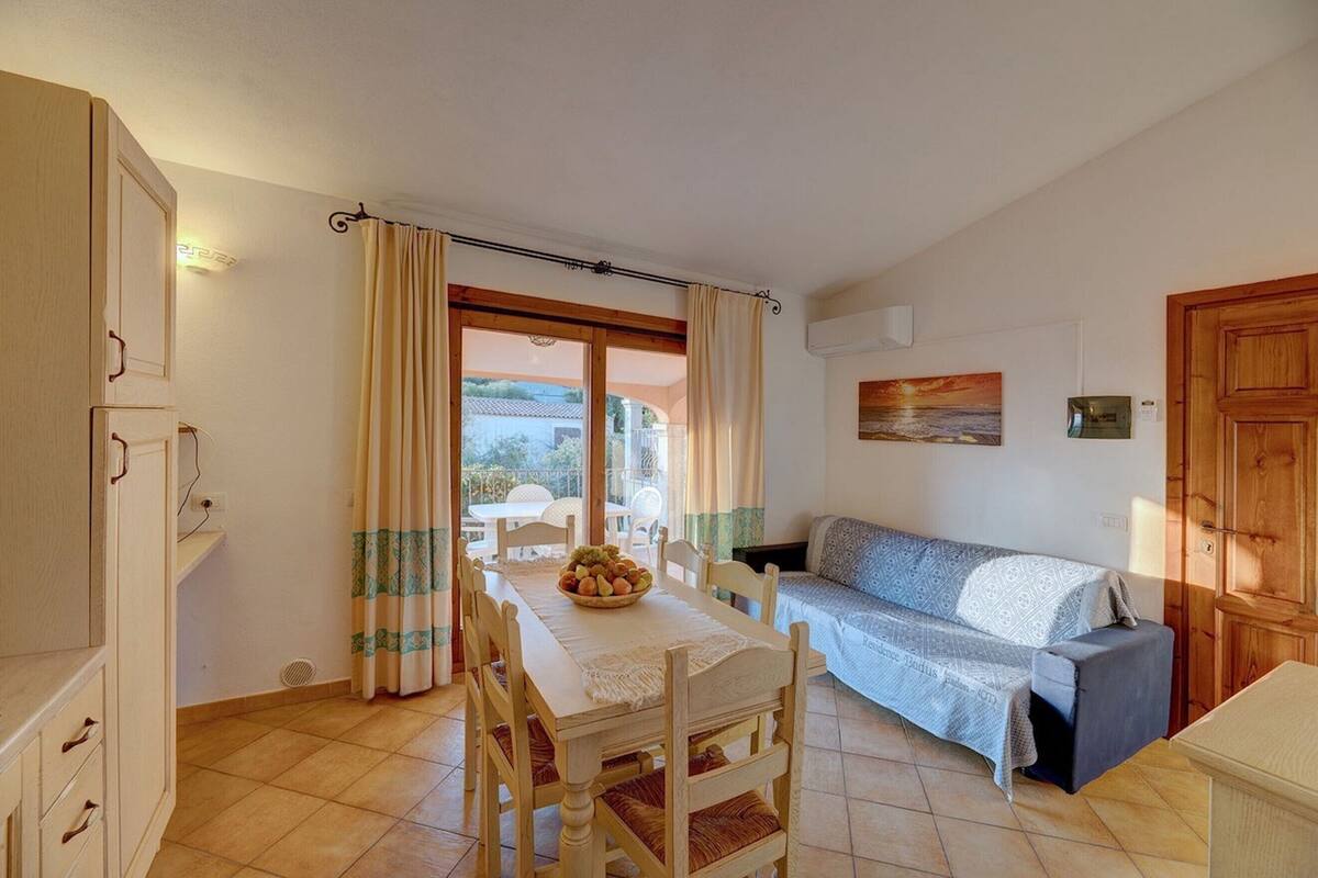 Uma área de jantar com mesa posta para dois, um sofá e vista para o exterior através de uma janela.