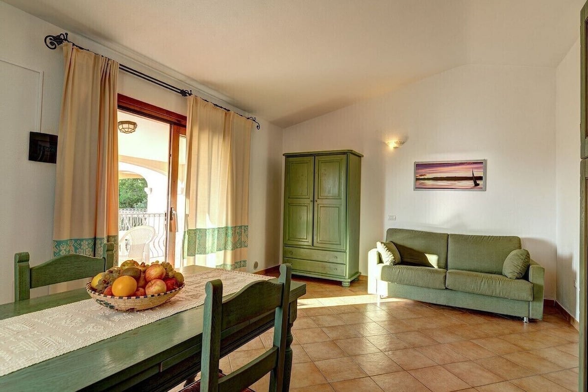 Uma sala de jantar com uma mesa posta para dois, um armário verde, um sofá verde e um quadro na parede.