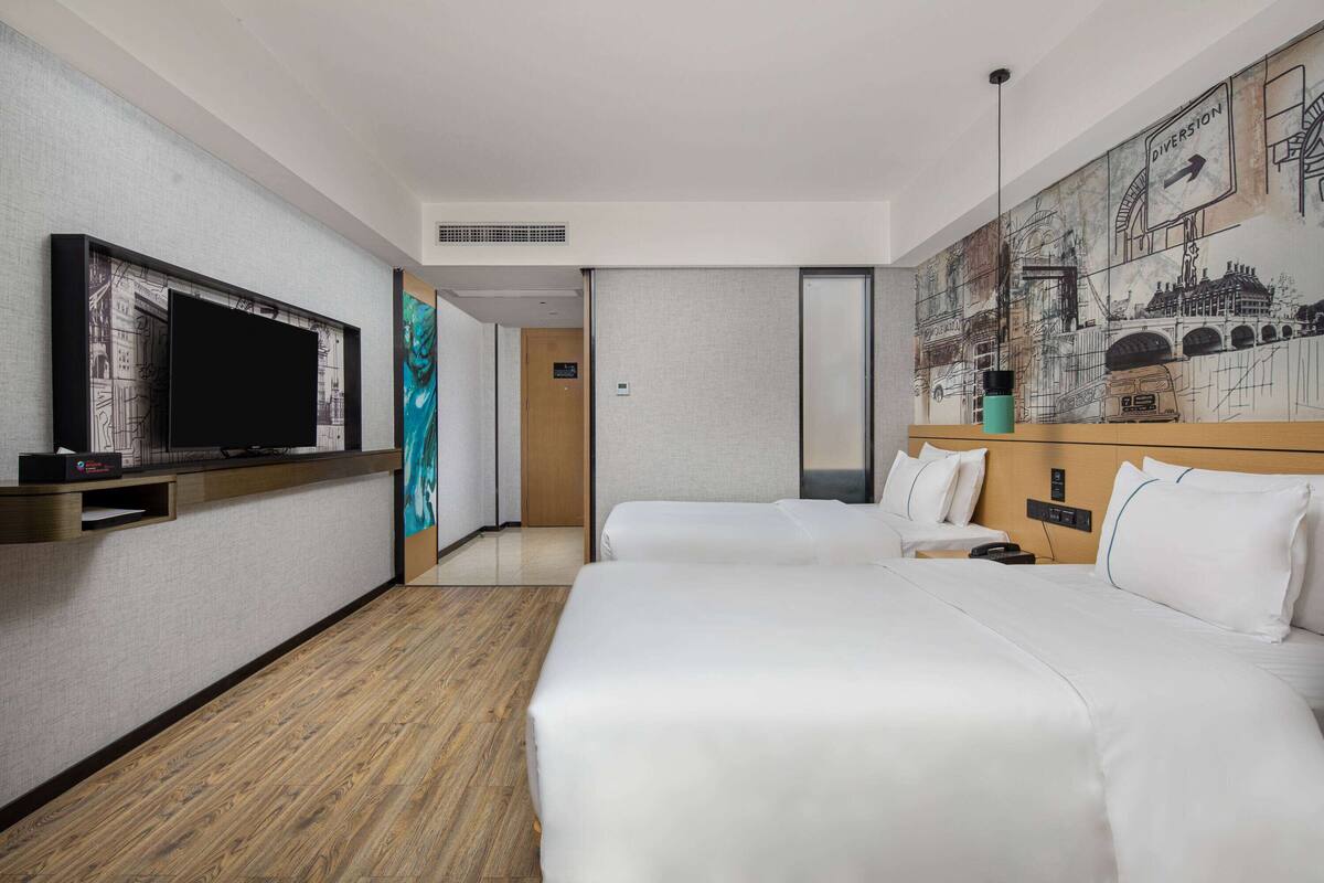 A hotel room with two beds, a flat-screen TV, a wooden floor, and a large wall mural.