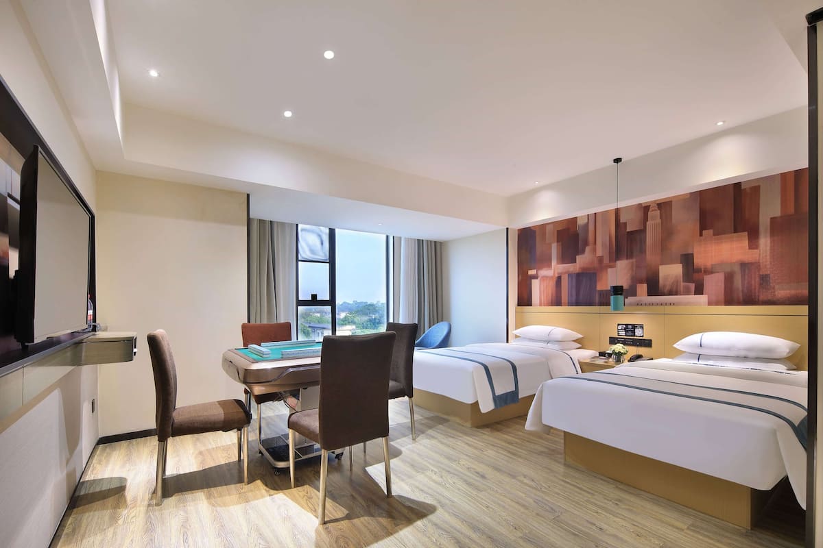A hotel room with a desk, two beds, a large window, and a cityscape view.