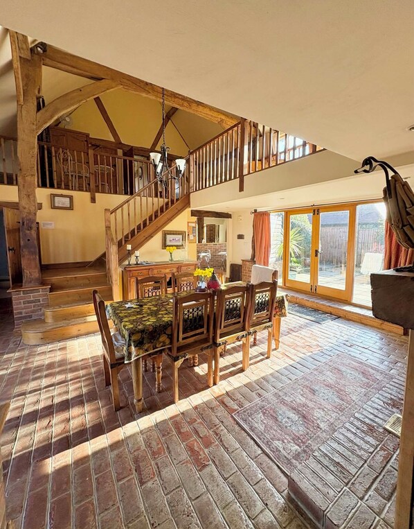 A spacious dining area with a wooden table and chairs, a staircase leading to an upper level, and a view of the outdoors through large glass doors.