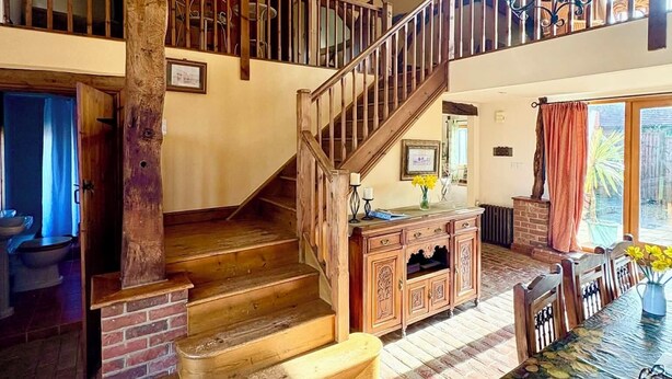 Un vaste loft doté de poutres apparentes, d’un escalier en bois, d’un coin repas avec une table et des chaises, et offrant une vue sur l’extérieur.