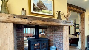 Une cheminée rustique, avec un foyer en briques, une cheminée en bois et, au-dessus, un tableau représentant un paysage encadré.