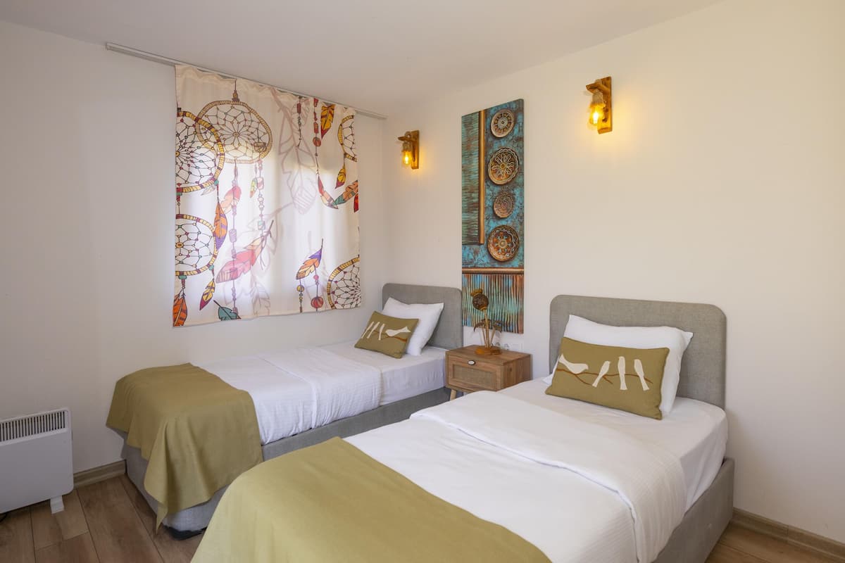 Habitación de hotel con dos camas individuales, un ventanal con cortina de atrapasueños, un aplique de pared y suelo de madera.