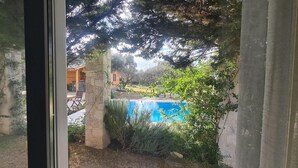 A view through a window of a stone pillar, a swimming pool, and a wooden building in the background. - Bir dem Urla (Urla)