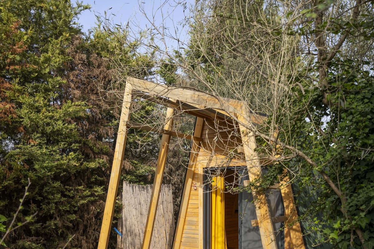 Una estructura de madera tipo cabaña con un porche de madera y una puerta con cortina amarilla.